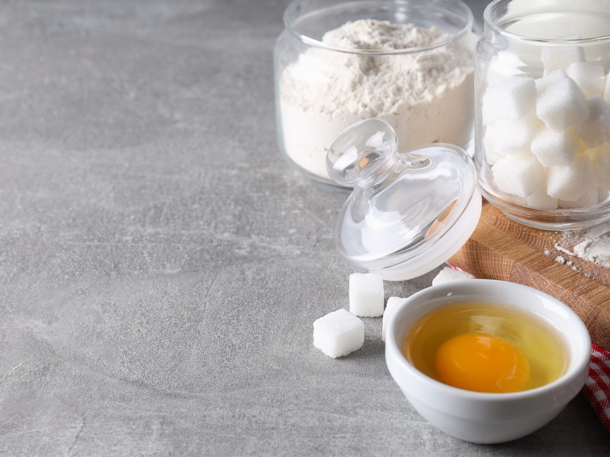 Baking station with flour, sugar cubes and a cracked egg in a bowl