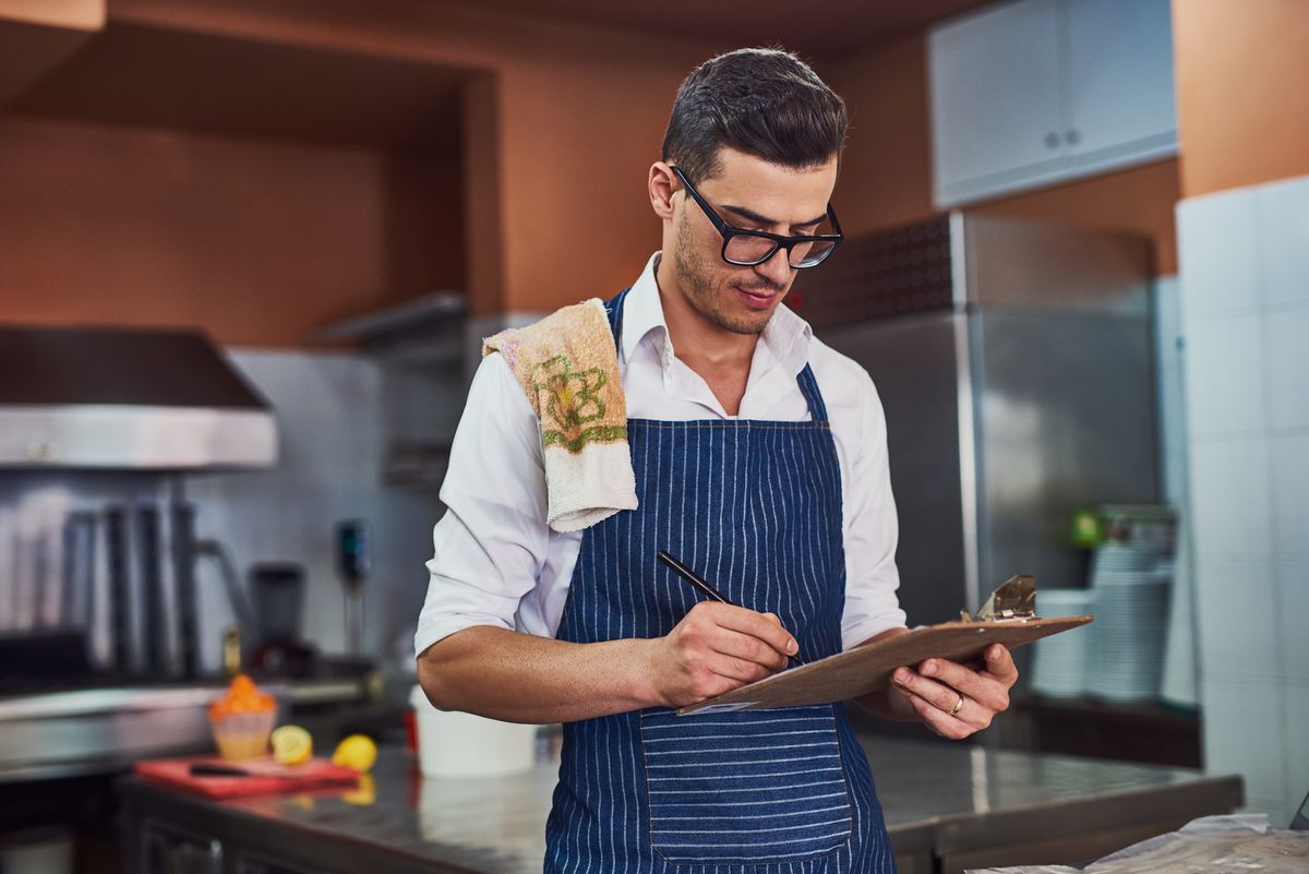 Chef taking inventory on a clipboard in a commercial kitchen
