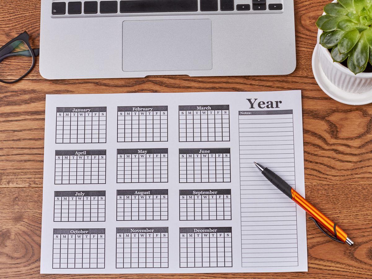 A year planner calendar, pen and laptop on a wooden desk