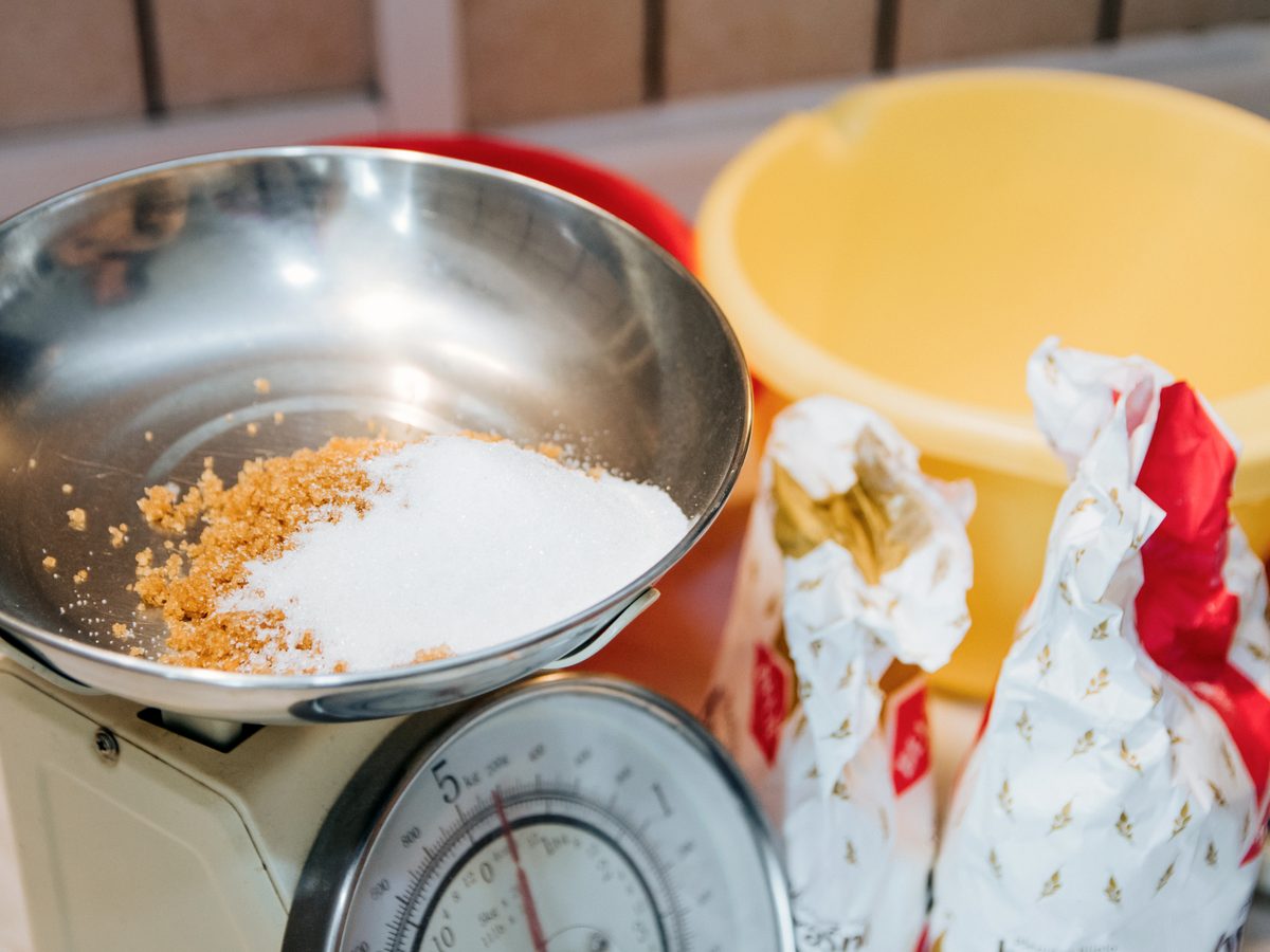 Brown and white sugar being weighed on a kitchen scale