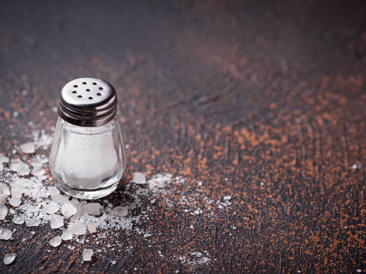 A salt shaker and scattered sea salt on a rust-coloured surface