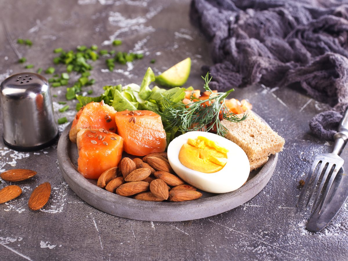 Plate of salmon, almonds, boiled egg and greens on a dark table