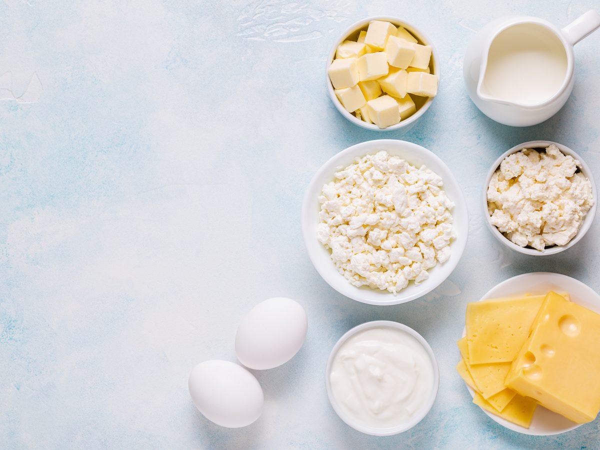 Overhead bowls of butter, cream, cheese, curd and eggs on a pale surface