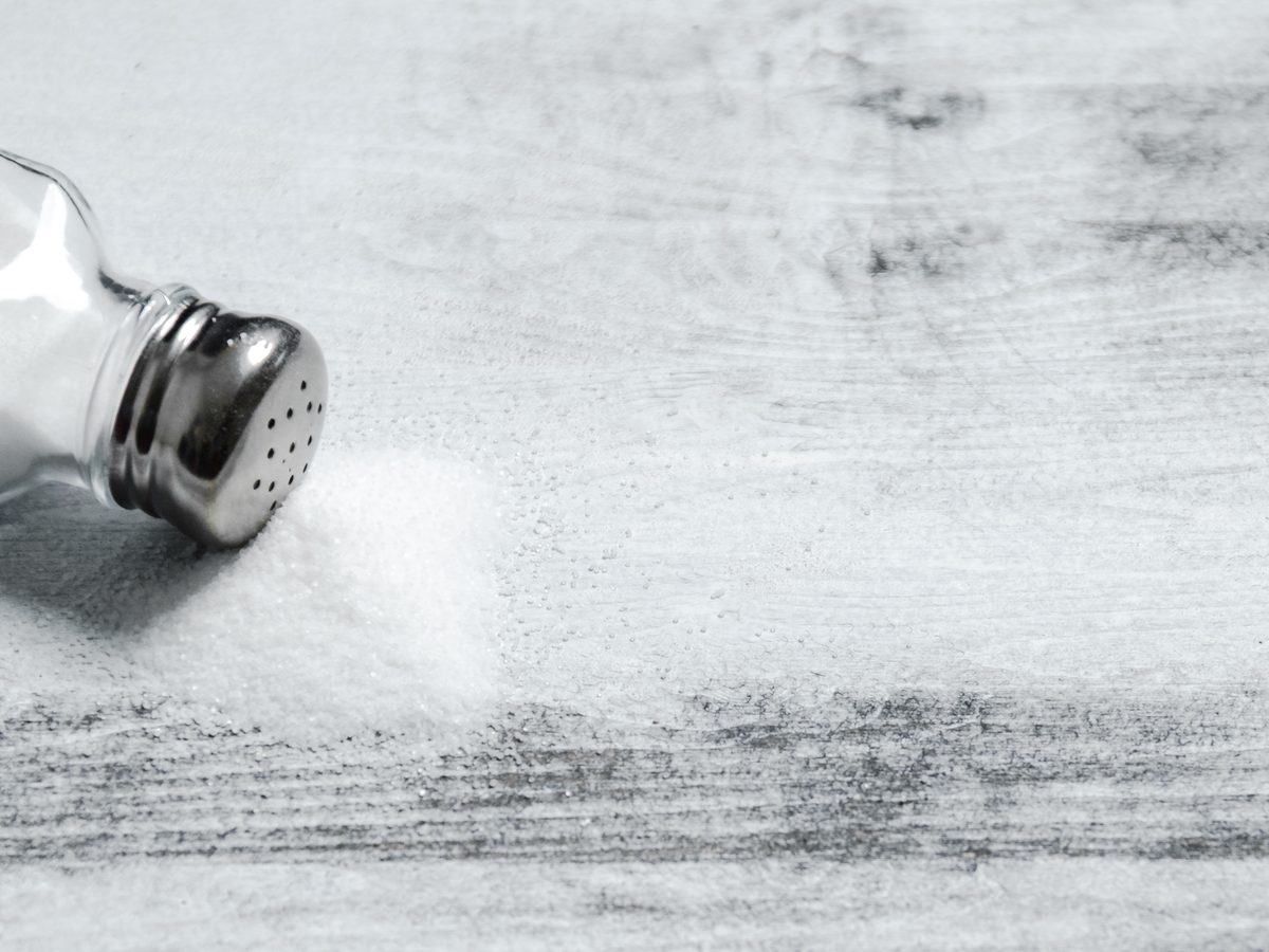 Tipped salt shaker spilling fine salt across weathered grey wood