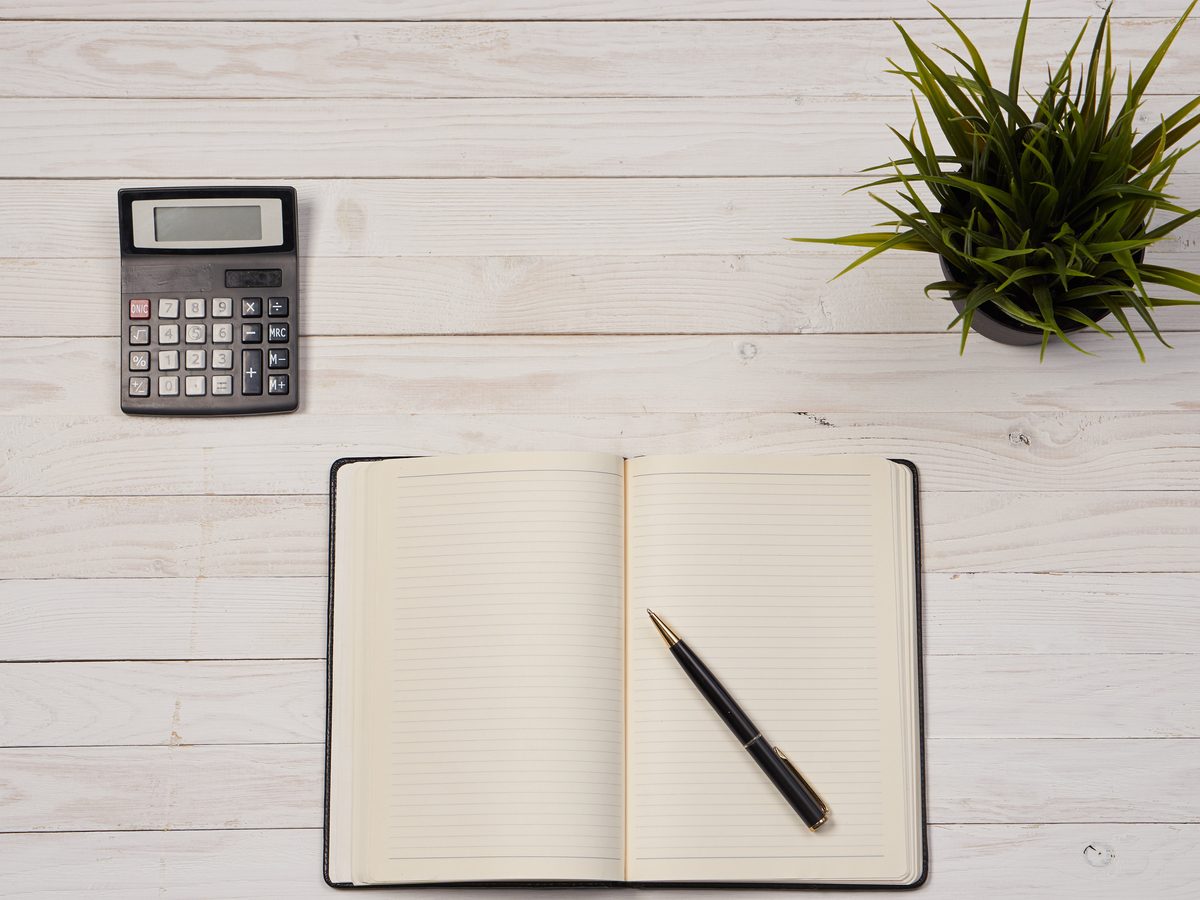 A calculator, open notebook and pen on a wooden desk