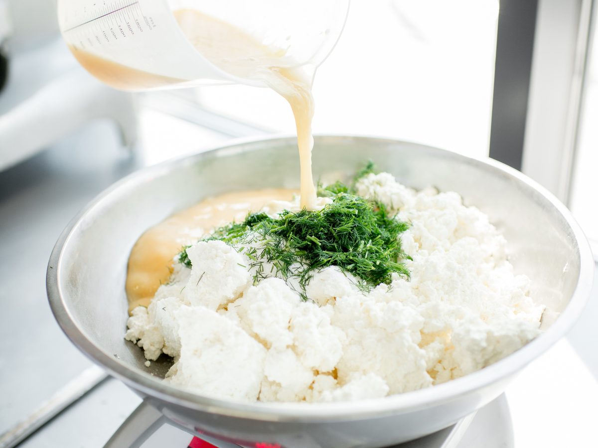 Cheese and herbs in a bowl on a kitchen scale while liquid is poured in
