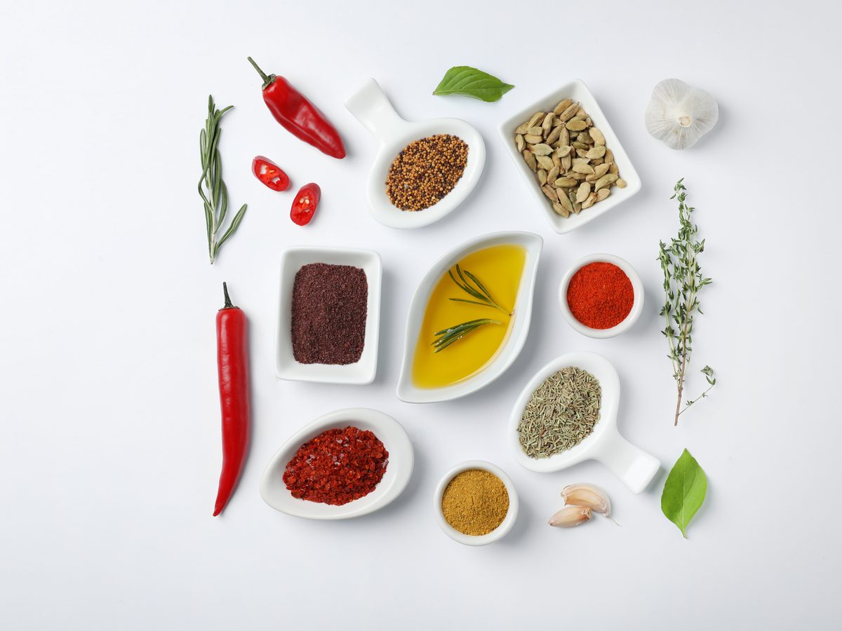 Small dishes of spices, oils, herbs and chillies arranged on white