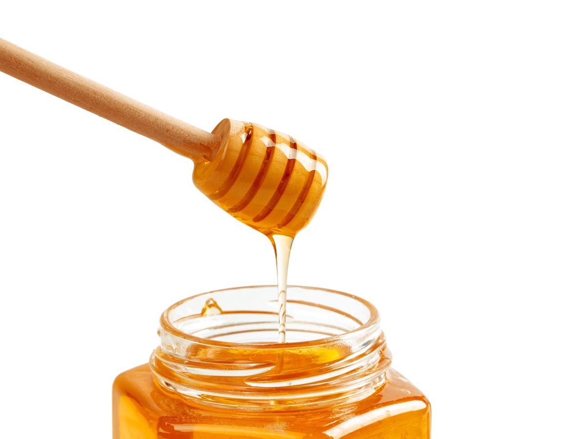 Honey dripping from a wooden dipper into an open jar