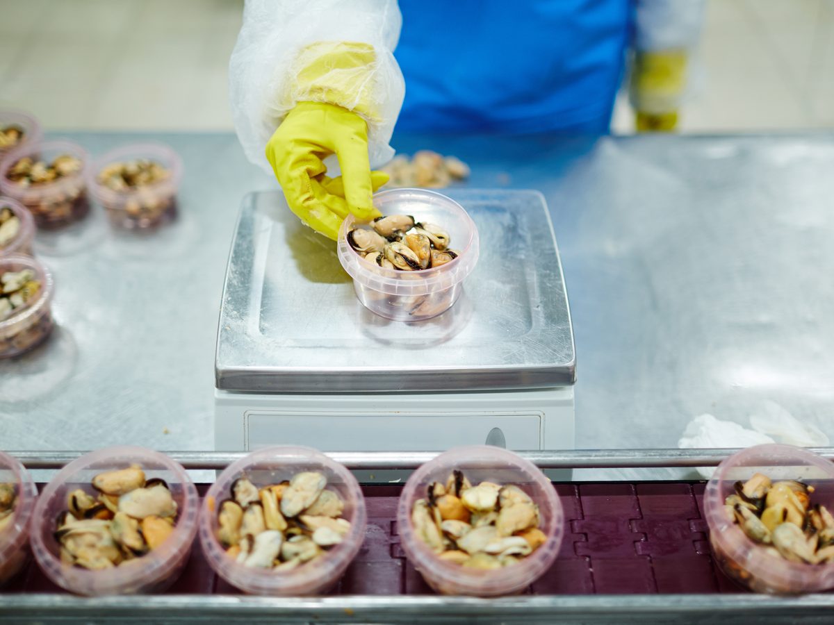 Worker weighing a tub of mixed nuts on a scale at a packing line