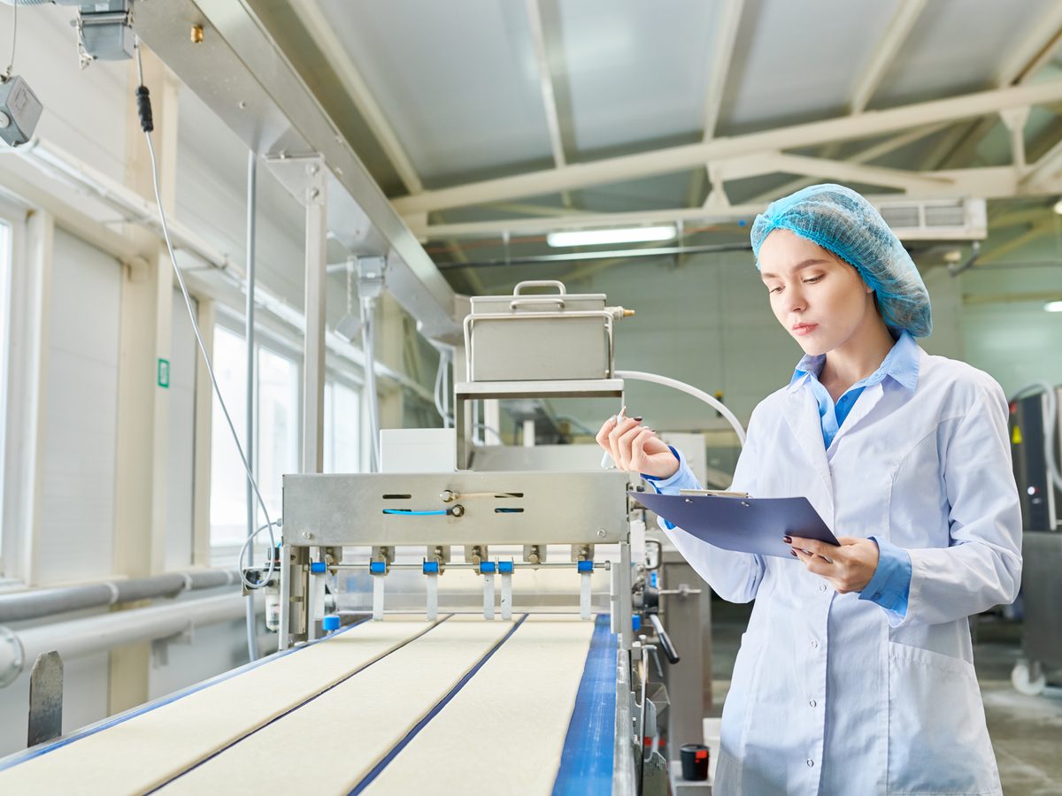 A quality inspector with a clipboard beside a food production line