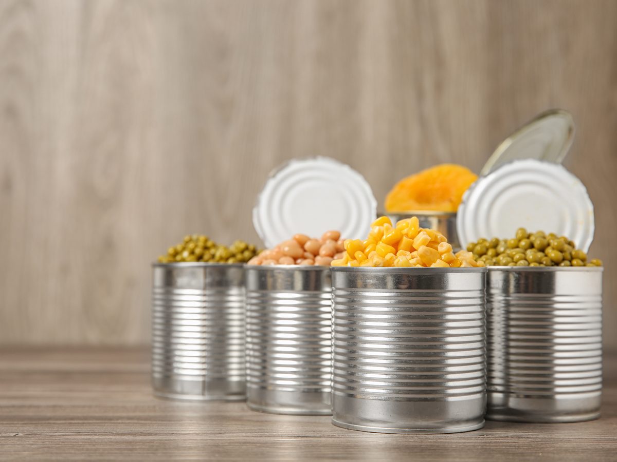 Open tin cans of peas, chickpeas and corn on a wooden counter