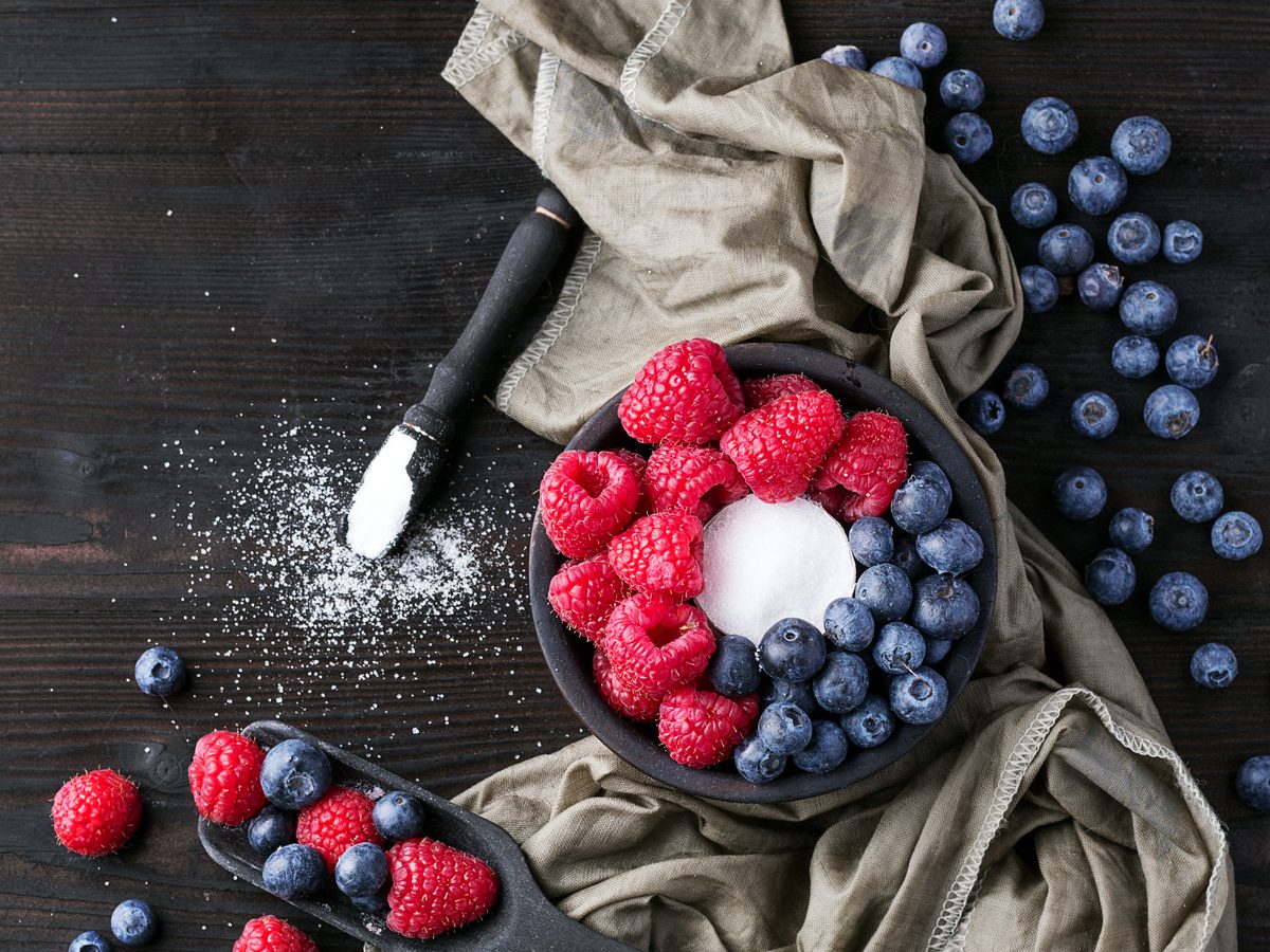 Bowl of raspberries and blueberries beside a scoop of white sugar