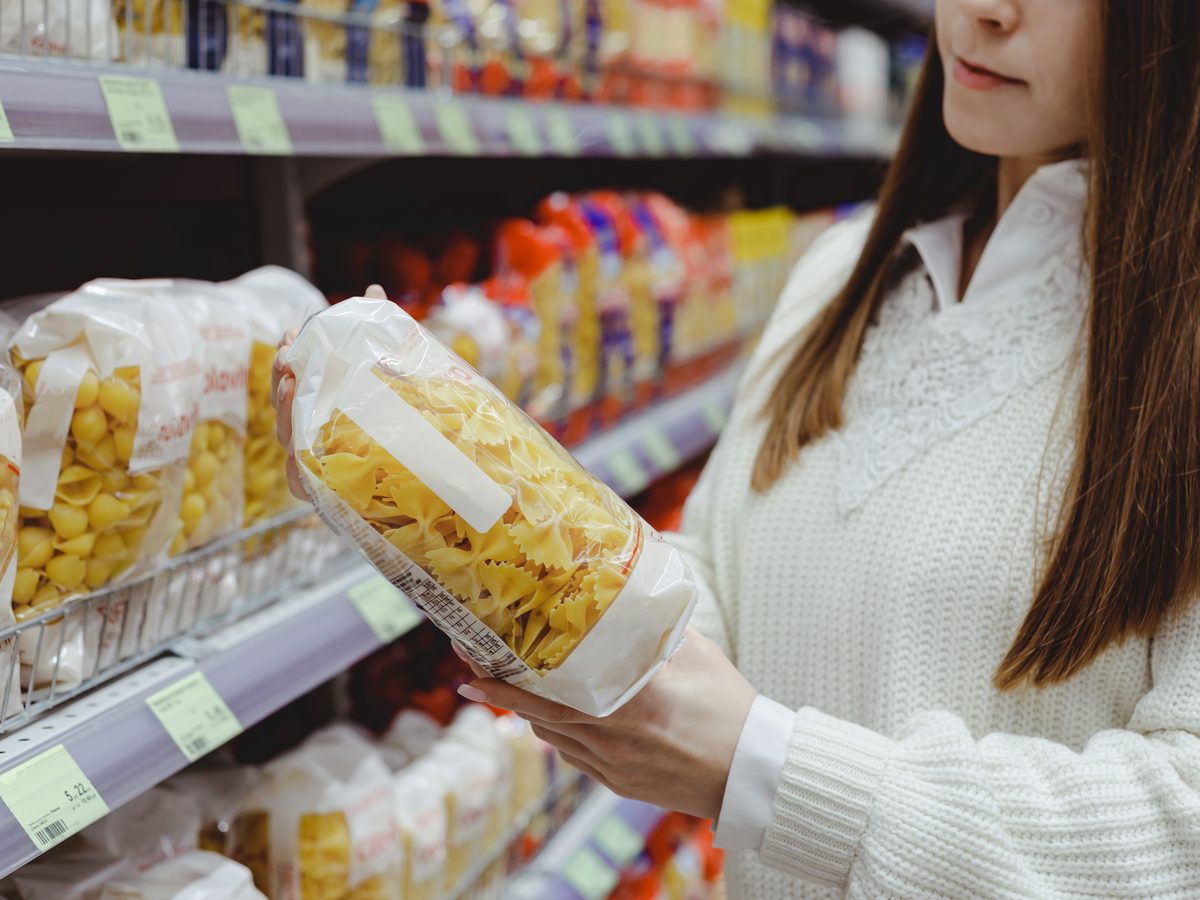 Shopper holding a bag of pasta in front of a supermarket shelf
